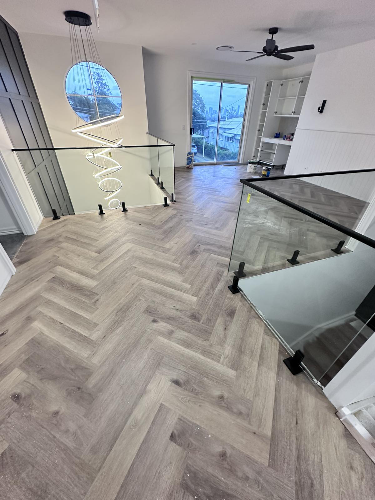 Upper landing with herringbone-pattern flooring and glass balustrade